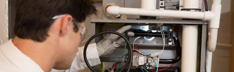 An Atlas Trillo technician wearing safety gloves and goggles is inspecting a furnace for service at a home in San Jose, CA.